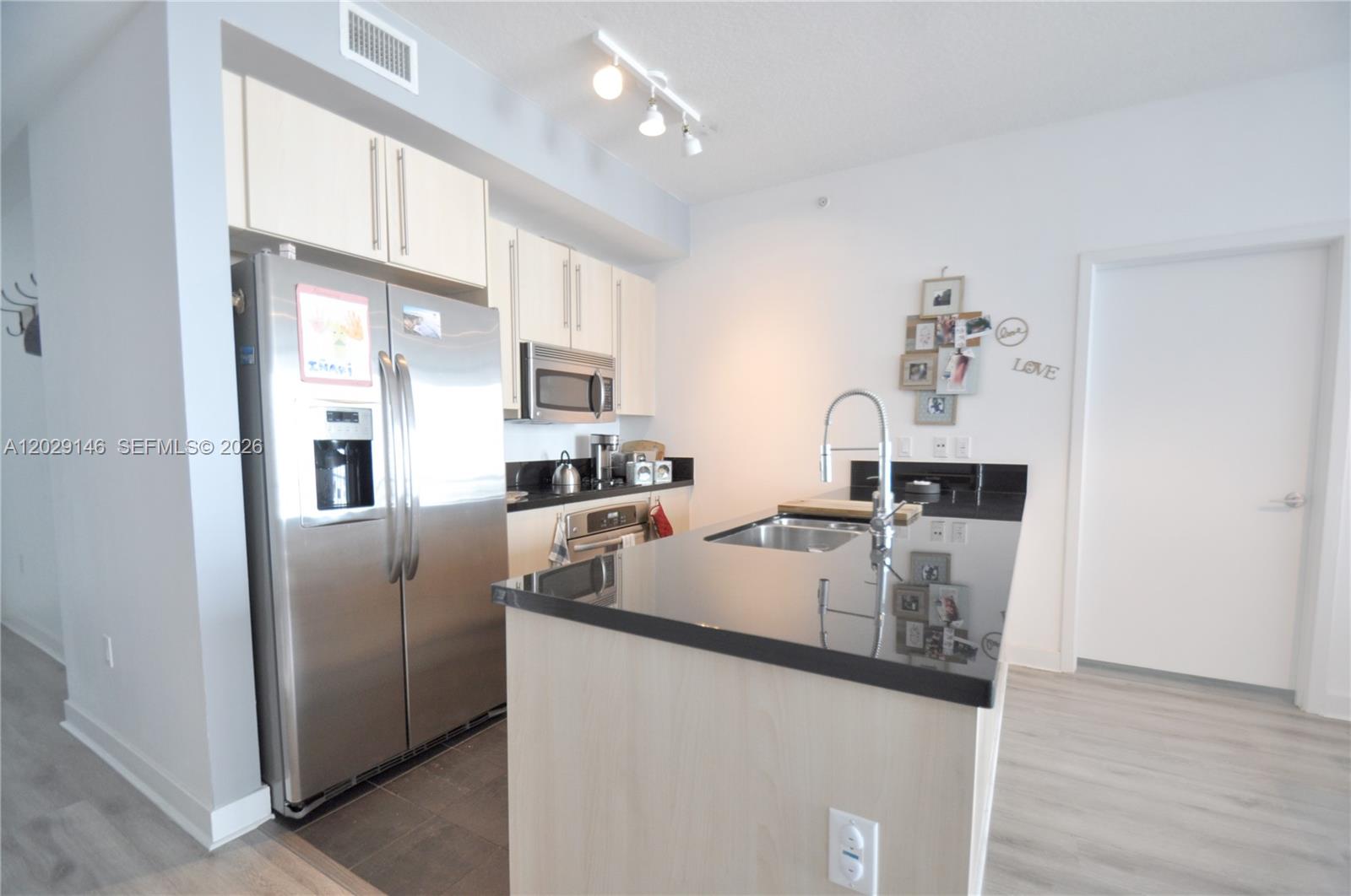 A kitchen features light wood cabinets, stainless steel appliances, and a black countertop island — 79 SW 12th St, Miami FL 33130, MIAMI, FL