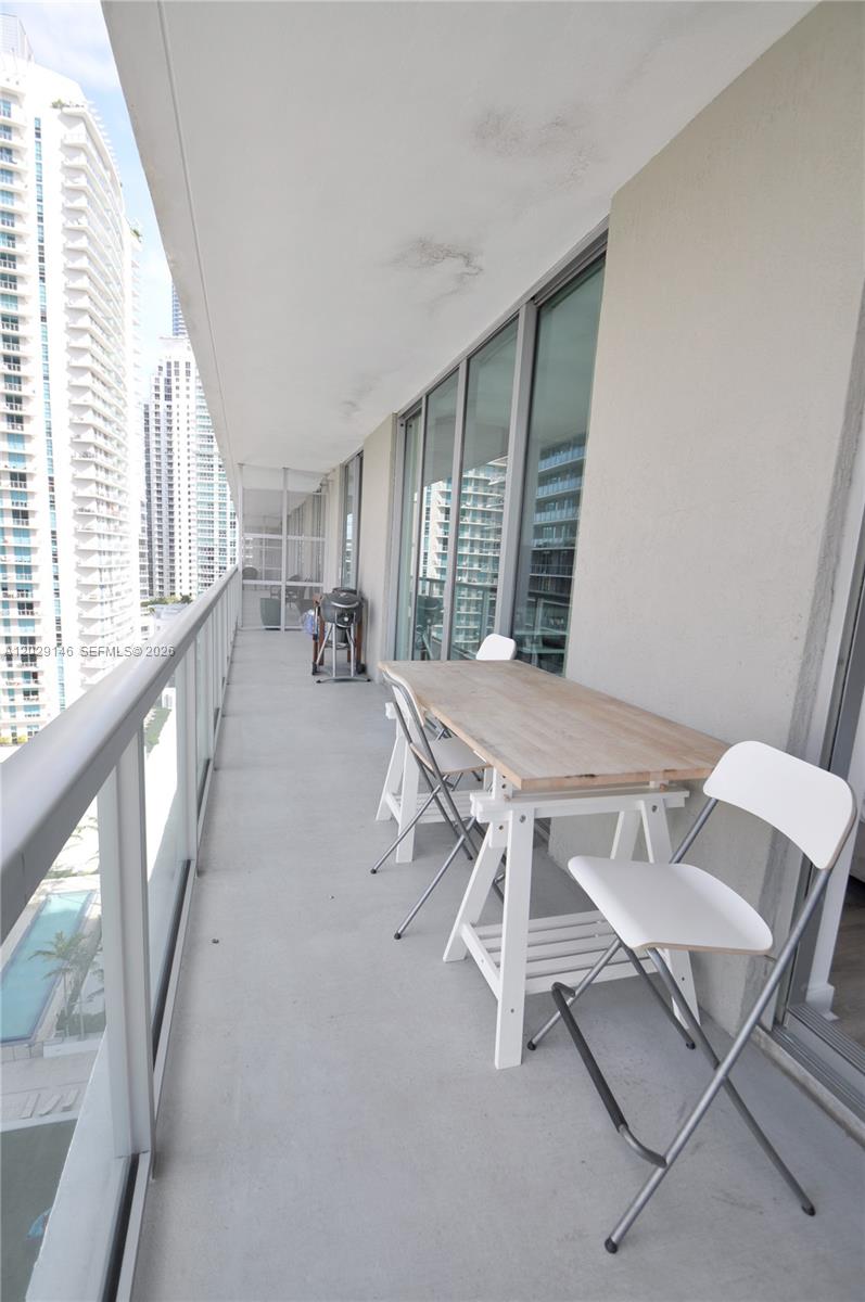 A high-rise balcony features a wooden table, white chairs, and views of surrounding buildings — 79 SW 12th St, Miami FL 33130, MIAMI, FL