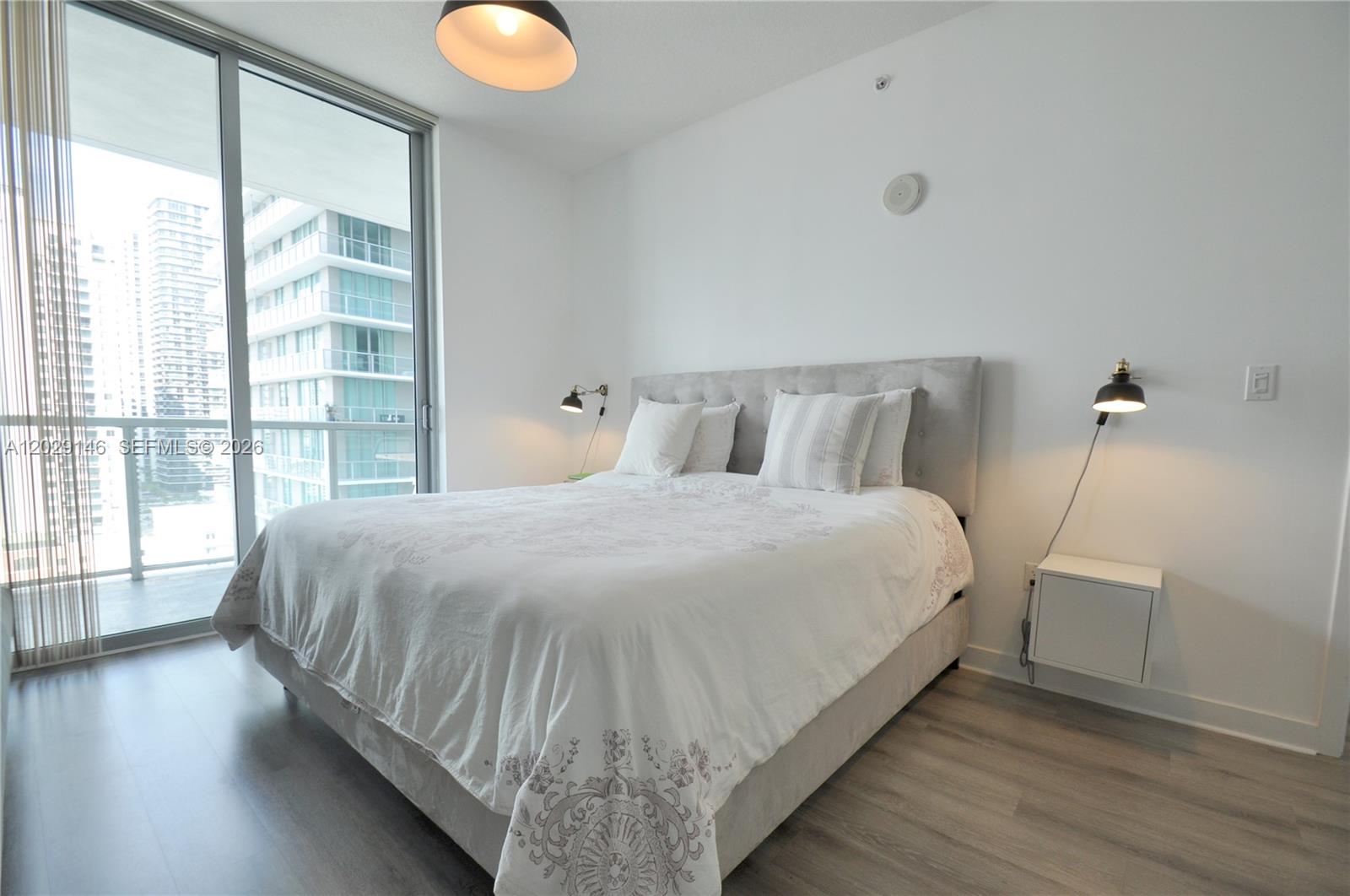 A bedroom features a gray upholstered bed, wall-mounted lamps, and a balcony with city views — 79 SW 12th St, Miami FL 33130, MIAMI, FL