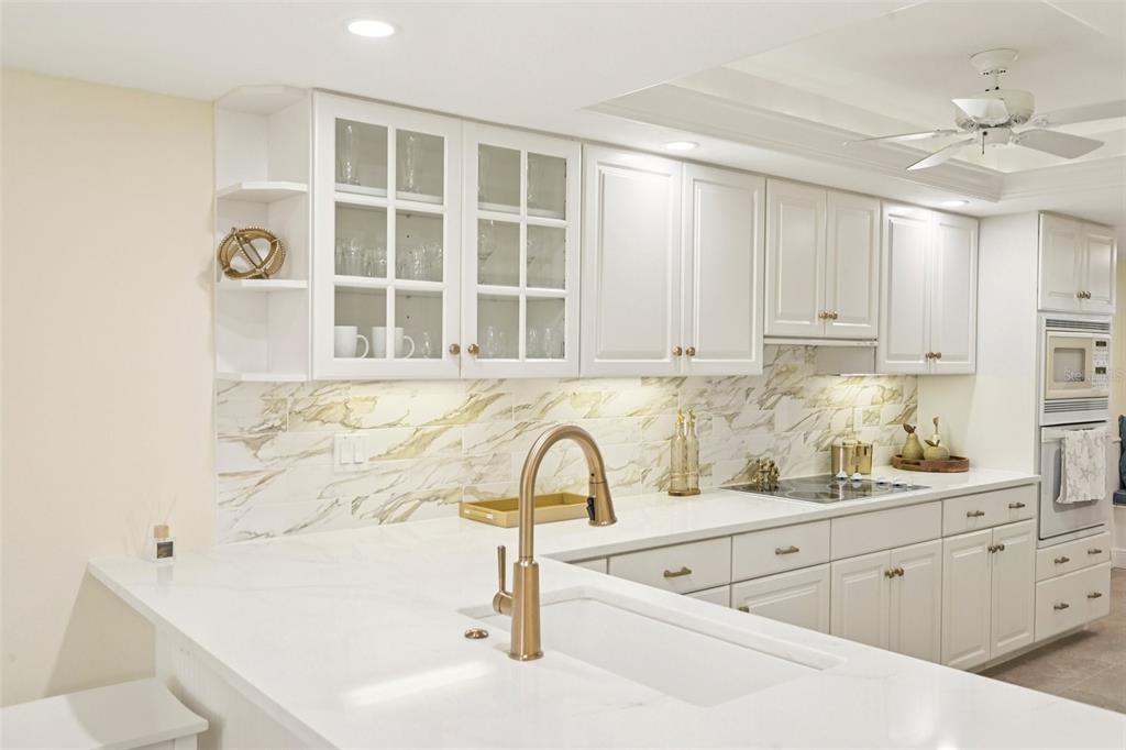 A kitchen features white cabinets, a marble backsplash, a gold faucet, and white countertops — 5780 MIDNIGHT PASS ROAD UNIT 407, SARASOTA, FL