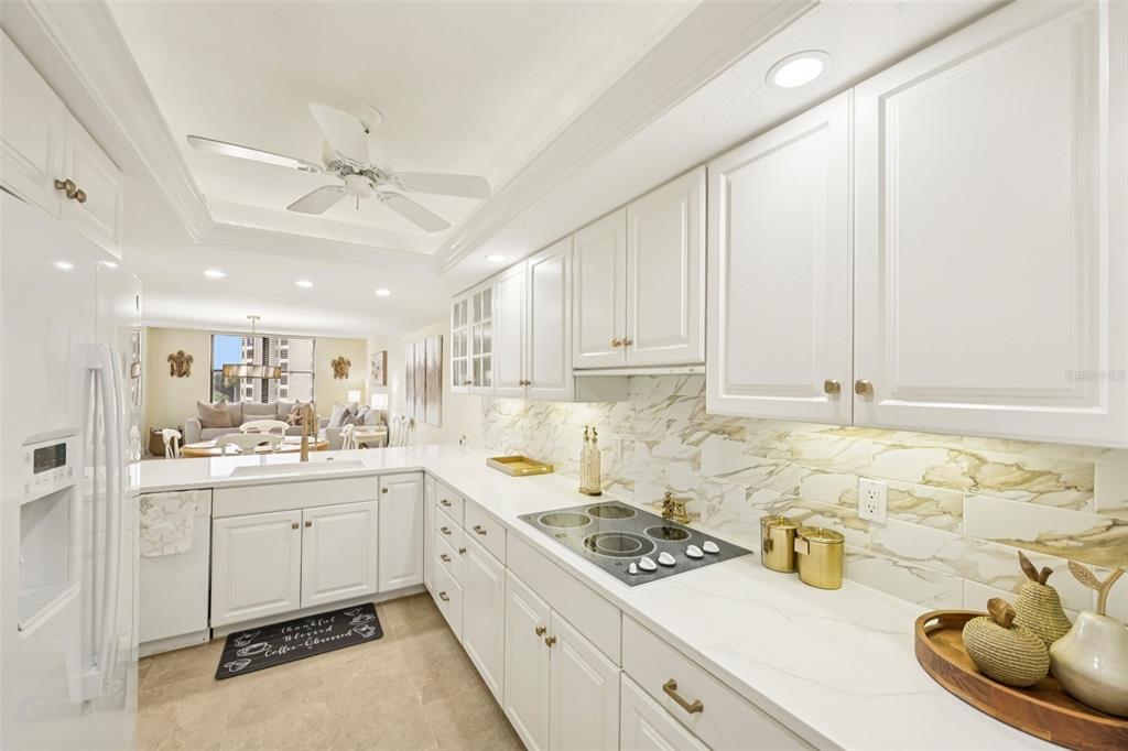 A white kitchen with marble-look backsplash, white cabinetry, and a view into the living area — 5780 MIDNIGHT PASS ROAD UNIT 407, SARASOTA, FL