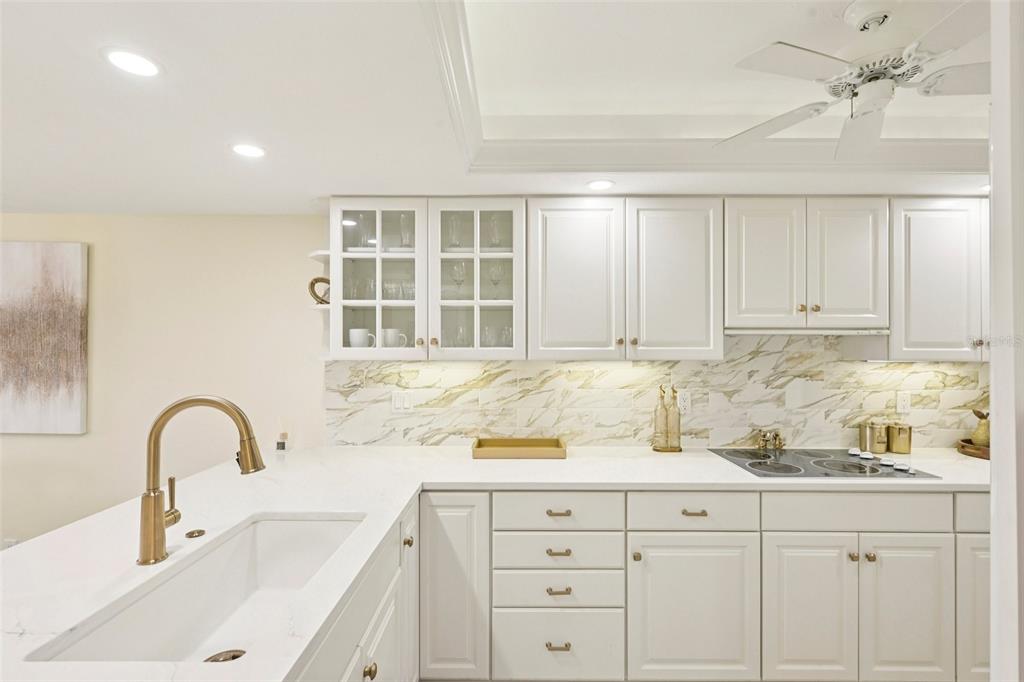 A white kitchen features marble-style countertops, gold hardware, glass-front cabinets, and a farmhouse sink — 5780 MIDNIGHT PASS ROAD UNIT 407, SARASOTA, FL