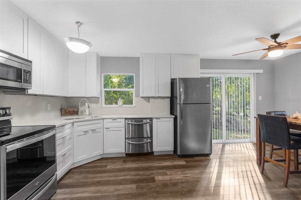 A kitchen features white cabinets, stainless steel appliances, wood-look flooring, and a sliding glass door — 16145 SNOW MEMORIAL HIGHWAY, BROOKSVILLE, FL