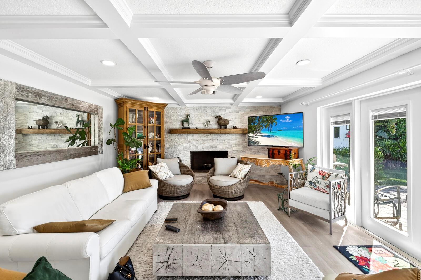 A living room features a white sofa, wicker armchairs, a stone fireplace, and a coffered ceiling — VERO BEACH, FL