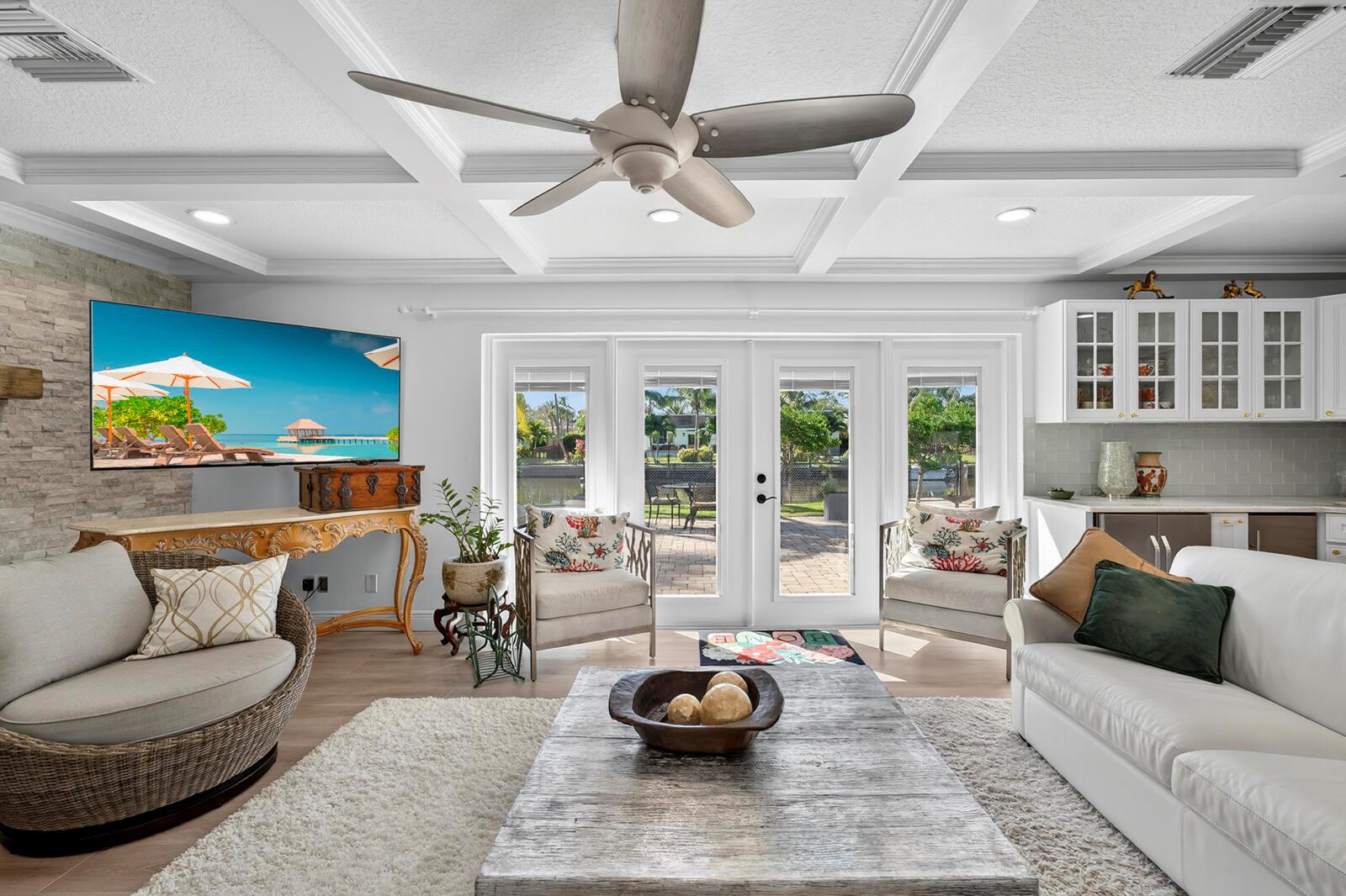 A living room features a coffered ceiling, stone accent wall, and glass doors overlooking water — VERO BEACH, FL