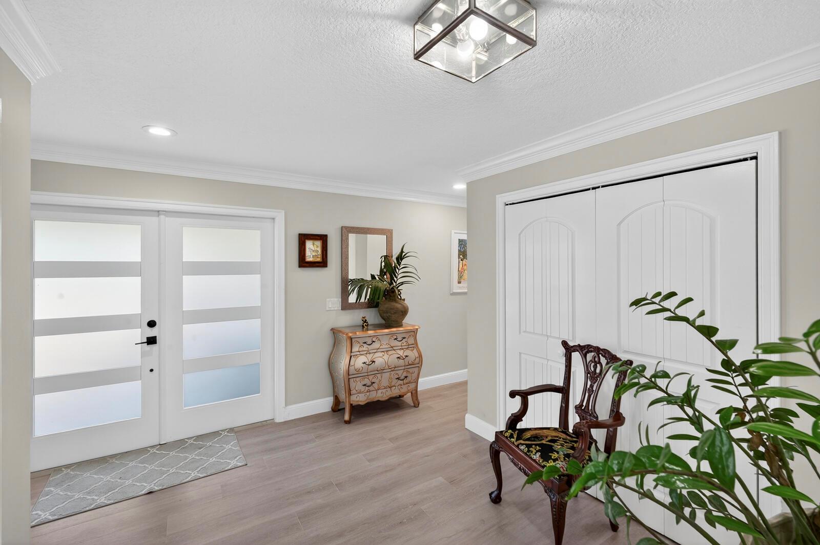 An entryway features light wood flooring, a decorative chest, a wooden chair, and double doors — VERO BEACH, FL