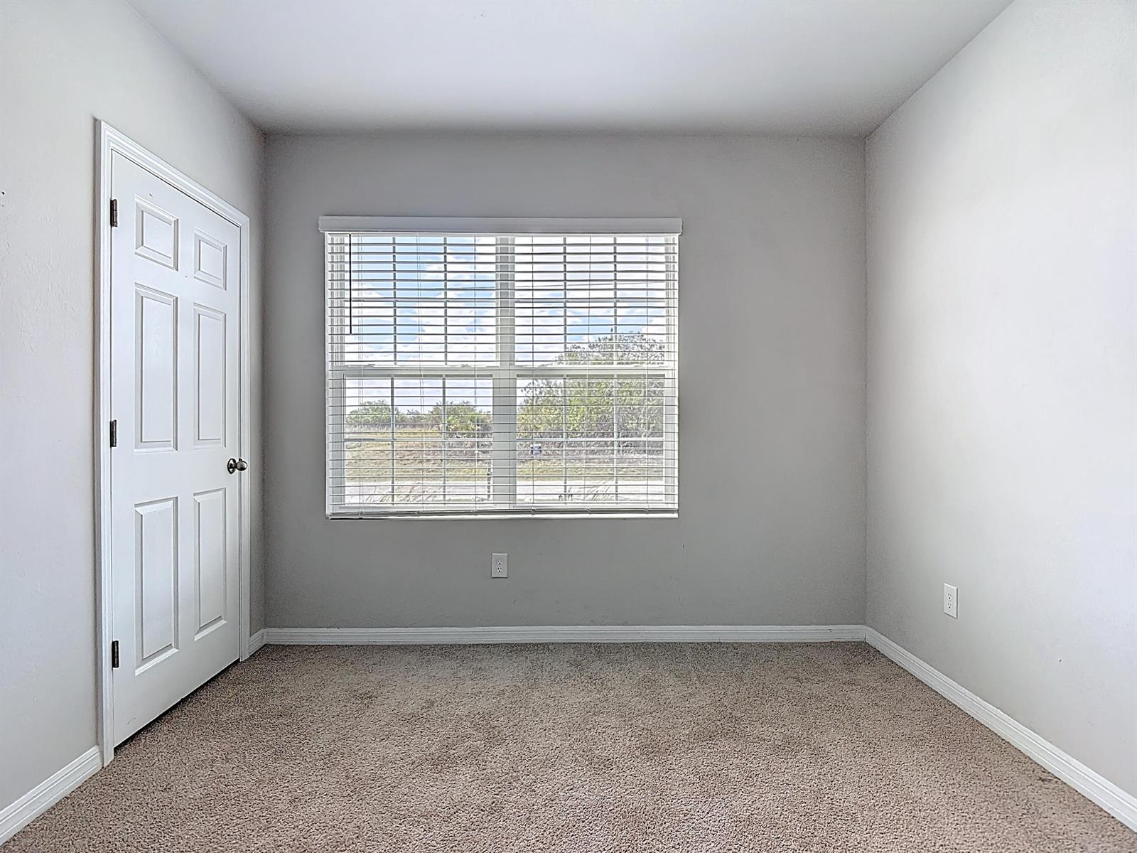 An empty bedroom features light gray walls, beige carpeting, a white door, and a window — 524 W Glendale Avenue, FL 33935, FL