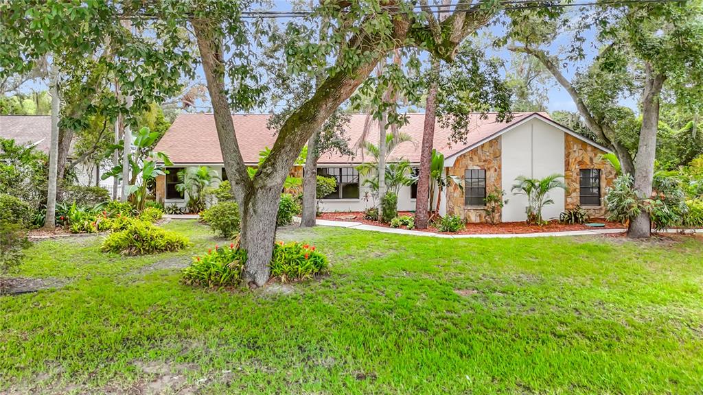 A single-story house with a stone facade, a brown roof, and mature trees in the yard — 12721 N ARMENIA AVENUE, TAMPA, FL