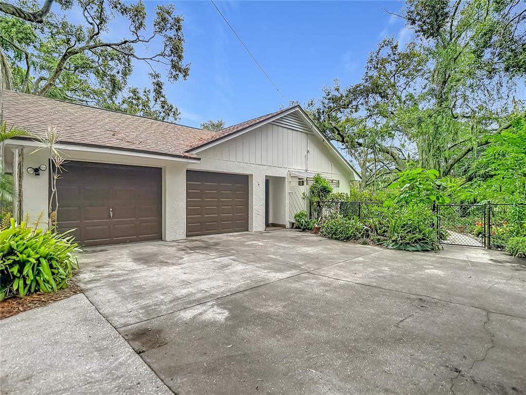 A two-car garage with brown doors and a concrete driveway sits beside a fenced yard — 12721 N ARMENIA AVENUE, TAMPA, FL
