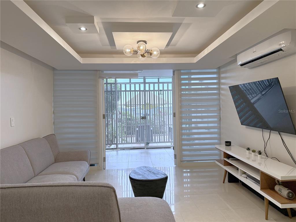 A living room features a grey sofa, white media console, and a view of a patio — 120 AVENIDA LA SIERRA UNIT F6102, SAN JUAN, PR