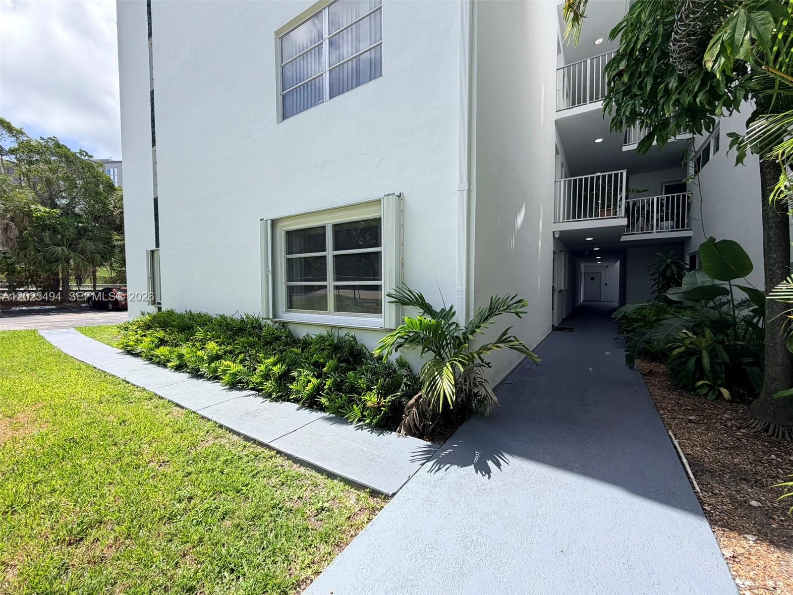 A white multi-story apartment building exterior features a gray walkway and landscaped garden beds — 9159 SW 77th Ave # 112, Miami FL 33156, MIAMI, FL