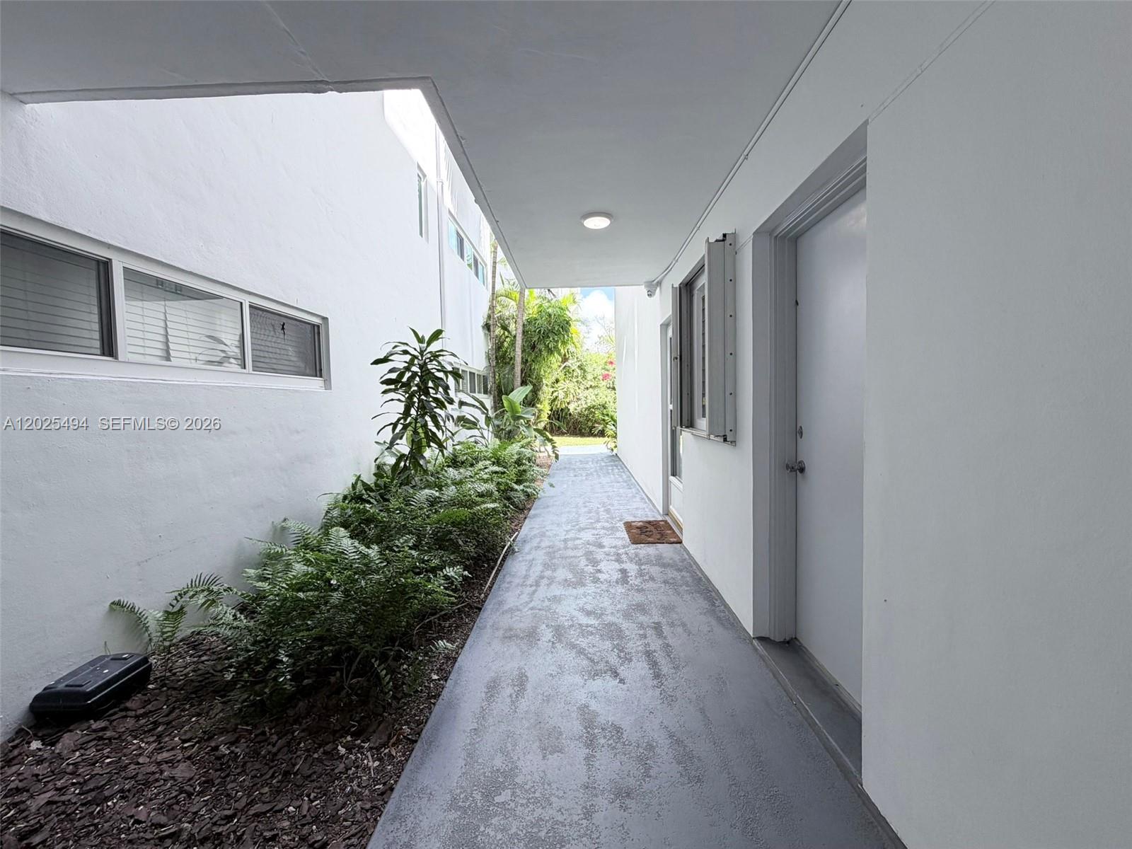 A narrow outdoor walkway leads between two white buildings with a small garden area — 9159 SW 77th Ave # 112, Miami FL 33156, MIAMI, FL