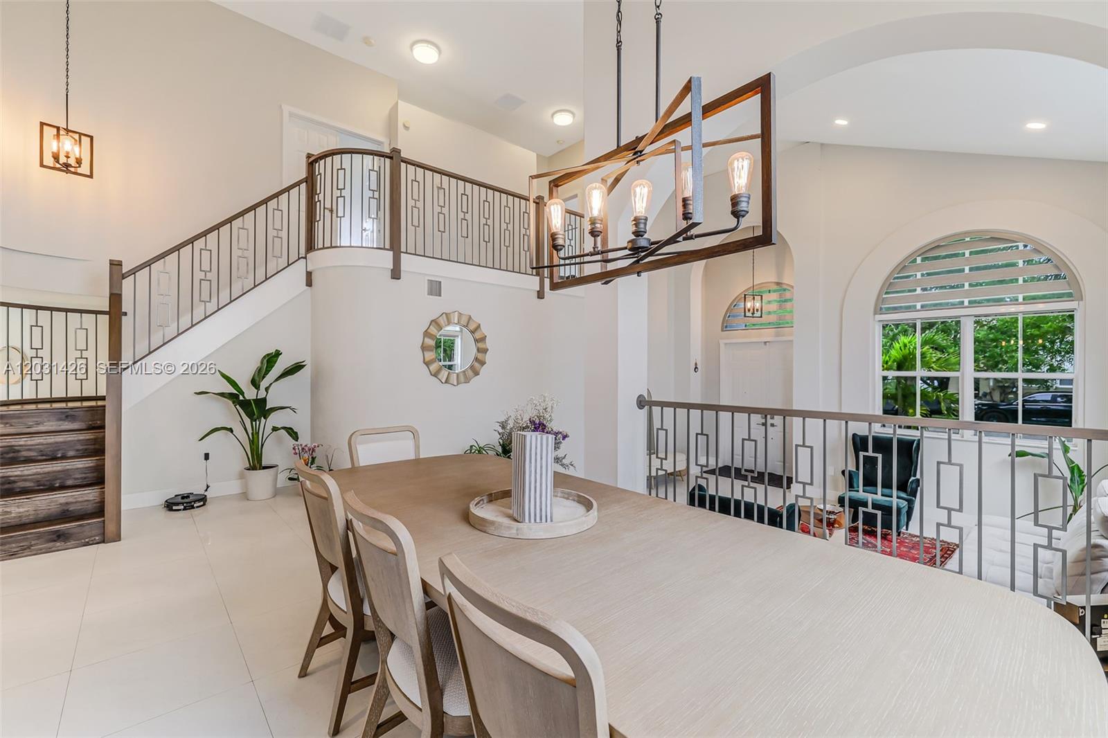 A dining area features a wooden table, modern chandelier, and an open staircase with metal railings — 15815 SW 52nd Ct, Miramar FL 33027, MIRAMAR, FL