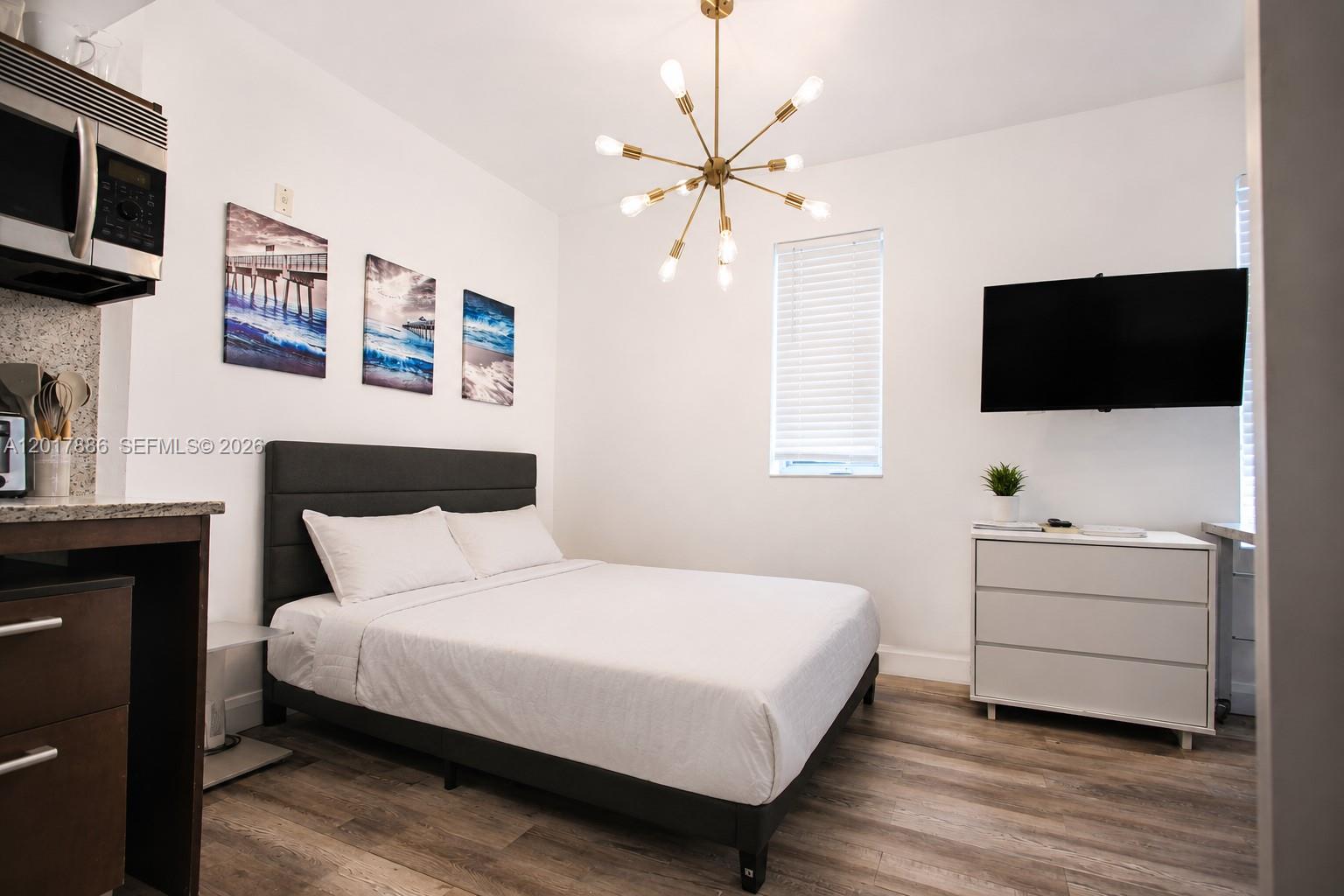 A bedroom features a bed, a dresser with a television, and a modern chandelier — 1036 Ocean Dr # B308, Miami Beach FL 33139, MIAMI BEACH, FL