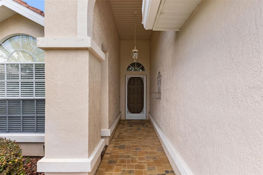 A covered entryway features a paved walkway leading to a front door with a screen — 9419 NEW ORLEANS DRIVE, WEEKI WACHEE, FL