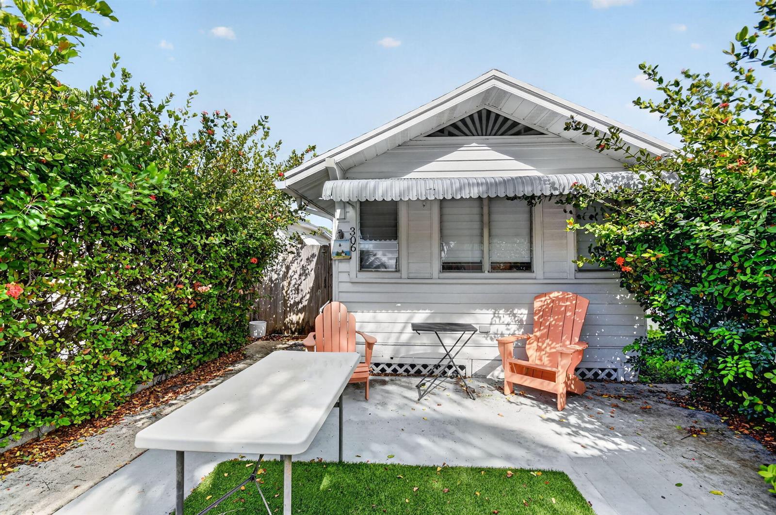 A small, light-gray cottage features a patio with two wooden chairs and a folding table — 306 N J Street, FL 33460, FL