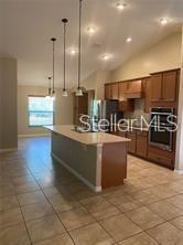 A kitchen features a central island with pendant lighting, wooden cabinetry, and tiled flooring — 104 S COOPERS HAWK WAY, PALM COAST, FL