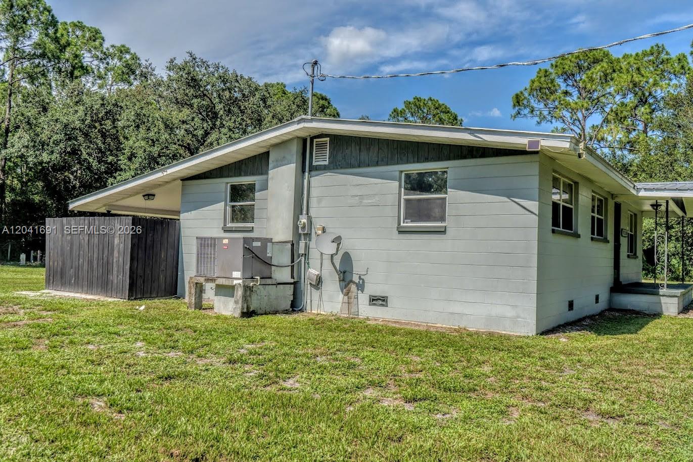 The exterior of a light gray house features a concrete block wall and HVAC unit — 1270 Nobles Rd, La Belle FL 33935, LA BELLE, FL