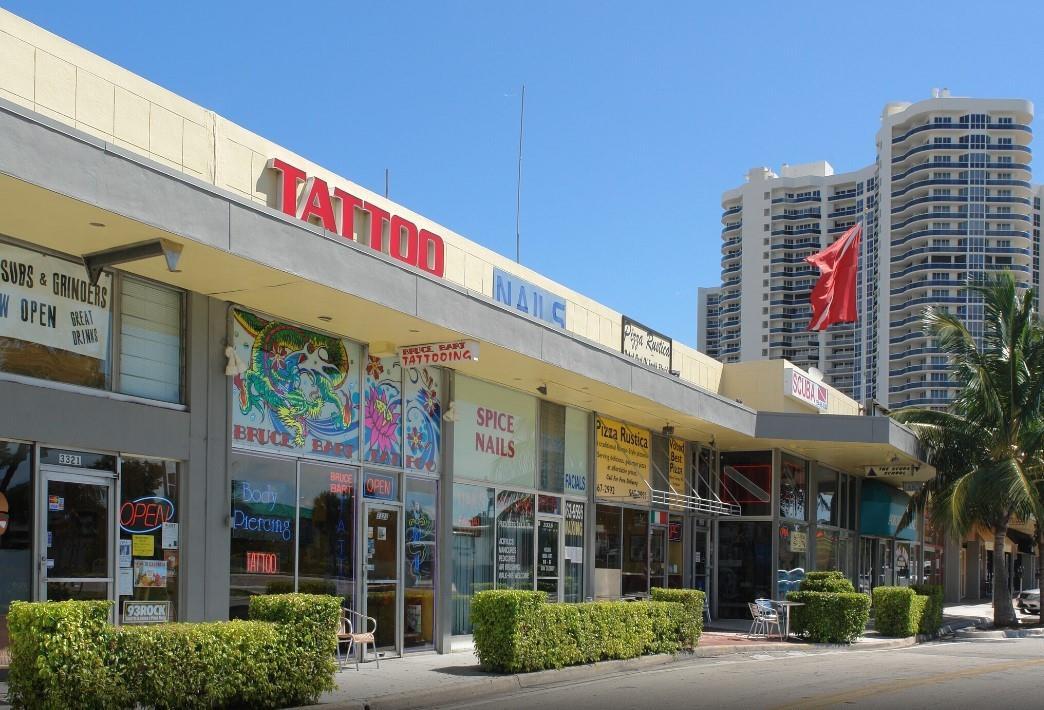 A street-level view of a commercial strip mall with a tattoo parlor and pizza restaurant — FORT LAUDERDALE, FL