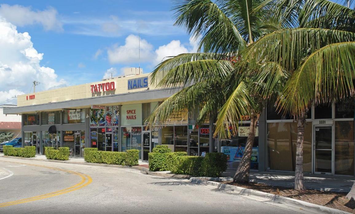 A single-story commercial strip mall with a tattoo parlor, nail salon, and palm trees — FORT LAUDERDALE, FL