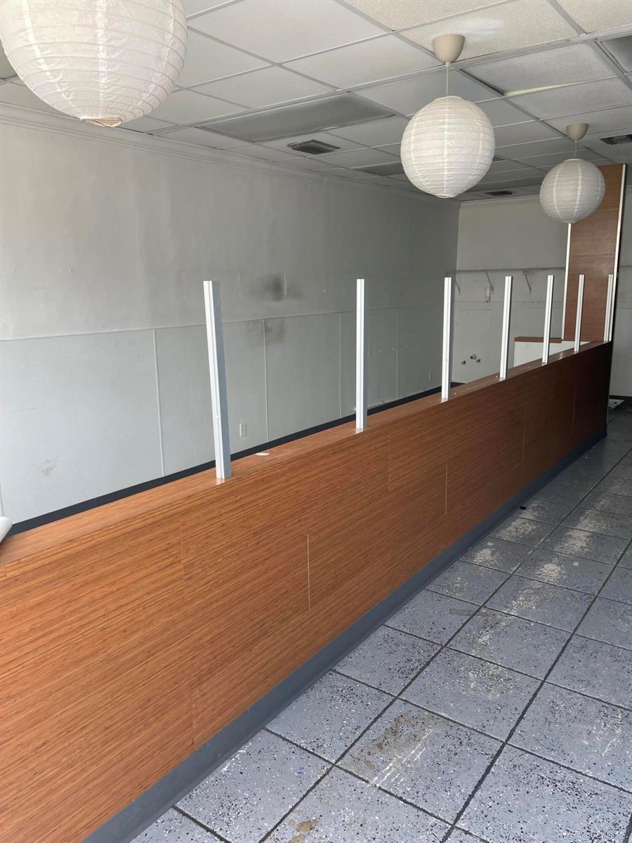An interior view shows a long wooden service counter with vertical glass partition supports — FORT LAUDERDALE, FL