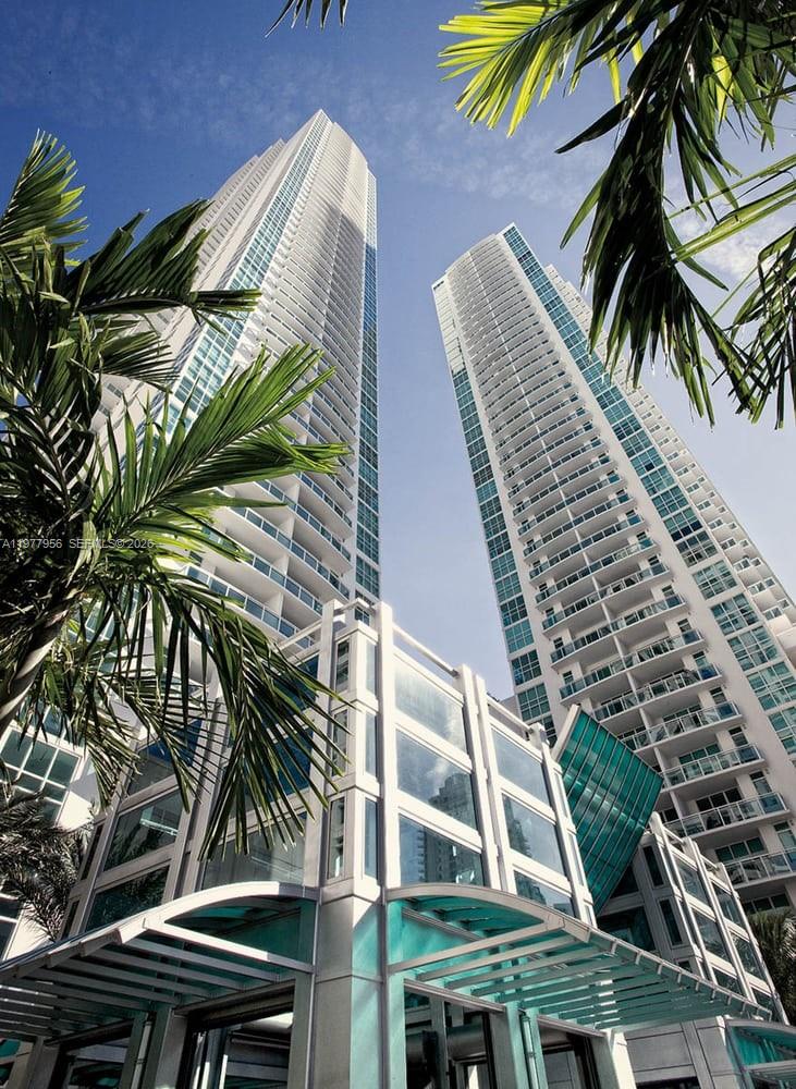 Low-angle view of two modern glass skyscrapers framed by palm tree fronds — 950 Brickell Bay Dr # 1107, Miami FL 33131, MIAMI, FL