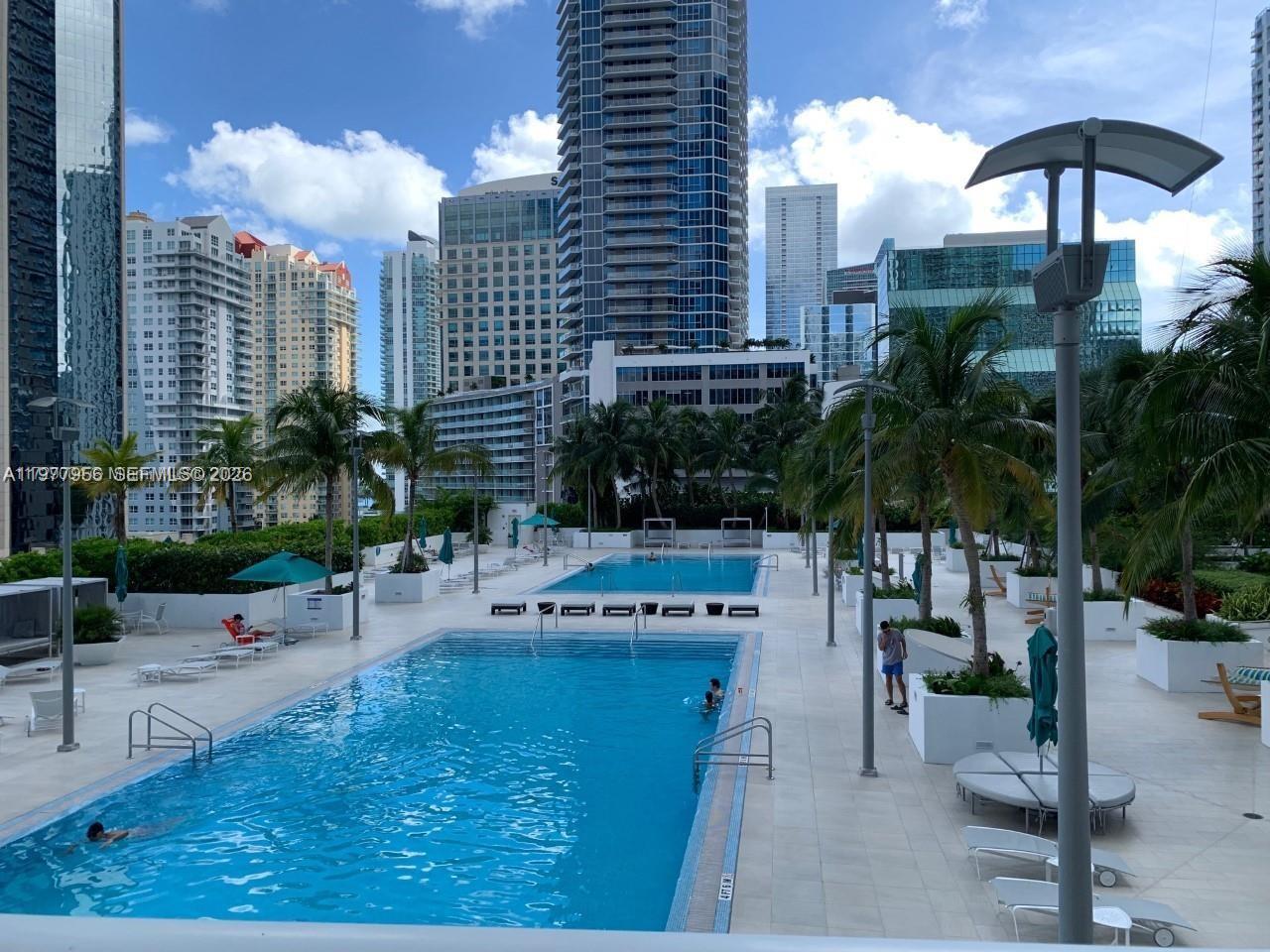 An outdoor swimming pool deck features lounge chairs, palm trees, and surrounding high-rise buildings — 950 Brickell Bay Dr # 1107, Miami FL 33131, MIAMI, FL