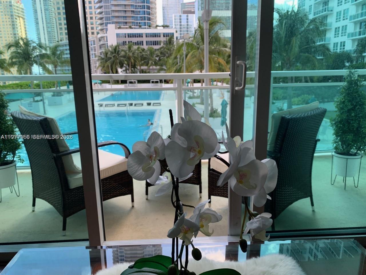 A white orchid sits on a table in front of a balcony overlooking a pool — 950 Brickell Bay Dr # 1107, Miami FL 33131, MIAMI, FL