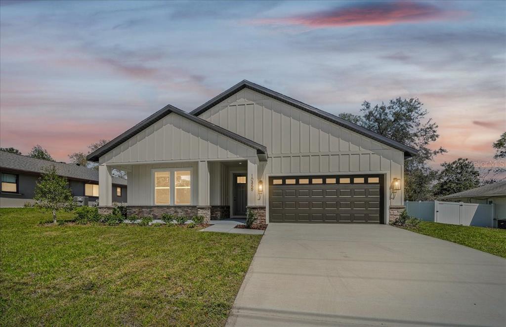 A single-story house with white vertical siding, a stone base, and a two-car garage — 10459 ABBEVILLE STREET, SPRING HILL, FL