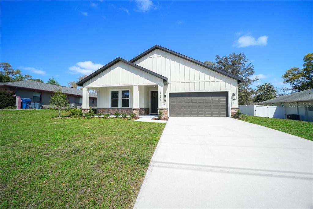 A single-story house with white vertical siding, a stone base, and a two-car garage — 10459 ABBEVILLE STREET, SPRING HILL, FL