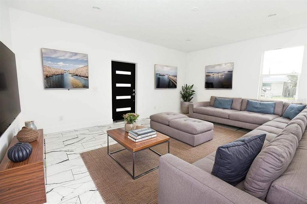A modern living room features a gray sectional sofa, a coffee table, and white tile floors — 67 W 10TH STREET, APOPKA, FL