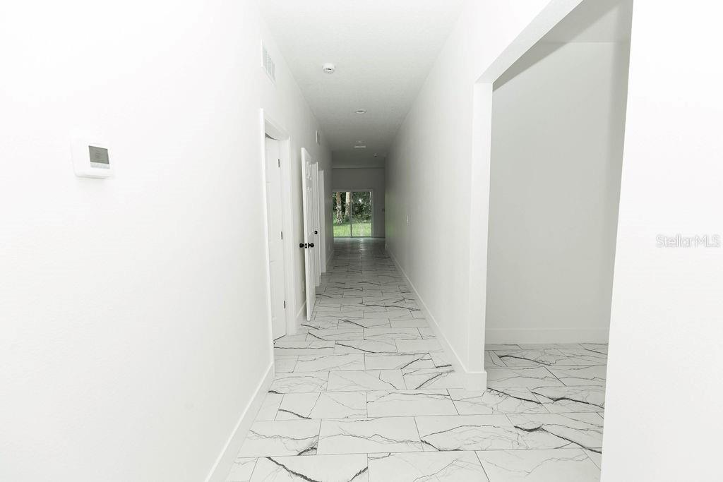 A long hallway with white walls and white marble-patterned tile flooring leads to a sliding door — 67 W 10TH STREET, APOPKA, FL