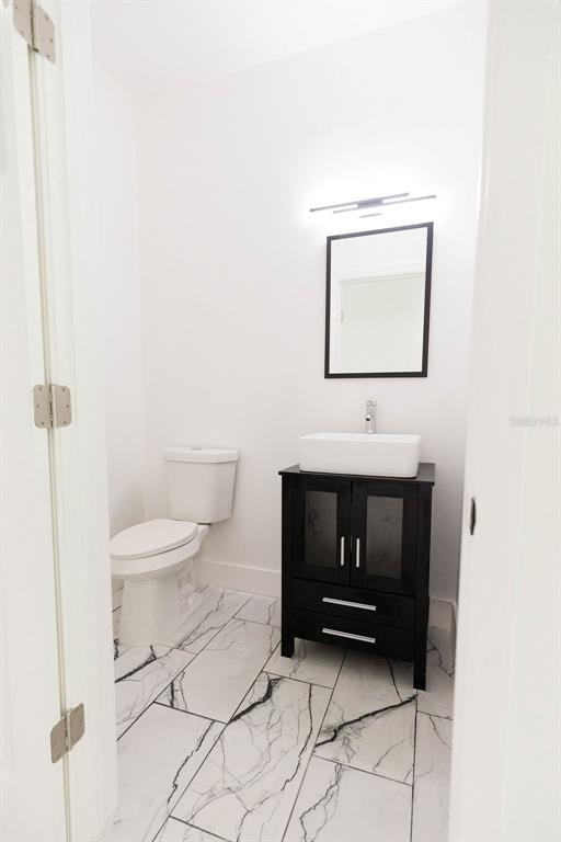 A small bathroom features a white toilet, a dark vanity with a vessel sink, and marble-look flooring — 67 W 10TH STREET, APOPKA, FL