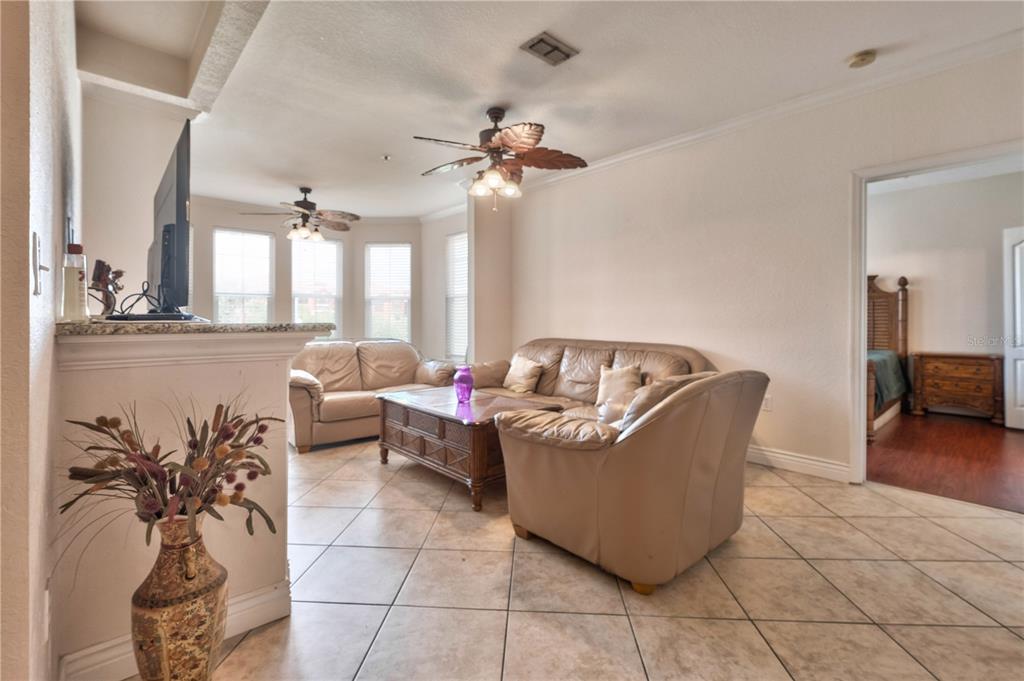 A living room with tile floors, leather furniture, and a ceiling fan near a bedroom — 2732 VIA MURANO UNIT 526, CLEARWATER, FL