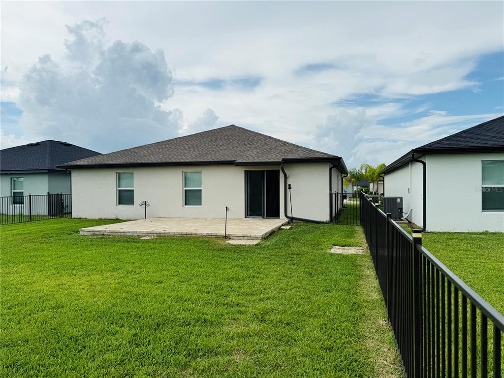 The rear exterior of a house features a paved patio, sliding glass doors, and fencing — 4034 SAN CLEMENTE COURT, NORTH FORT MYERS, FL