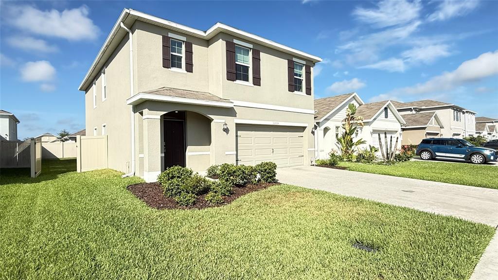 A two-story suburban house with a tan stucco exterior, brown shutters, and a two-car garage — 32724 ANSLEY BLOOM LANE, WESLEY CHAPEL, FL
