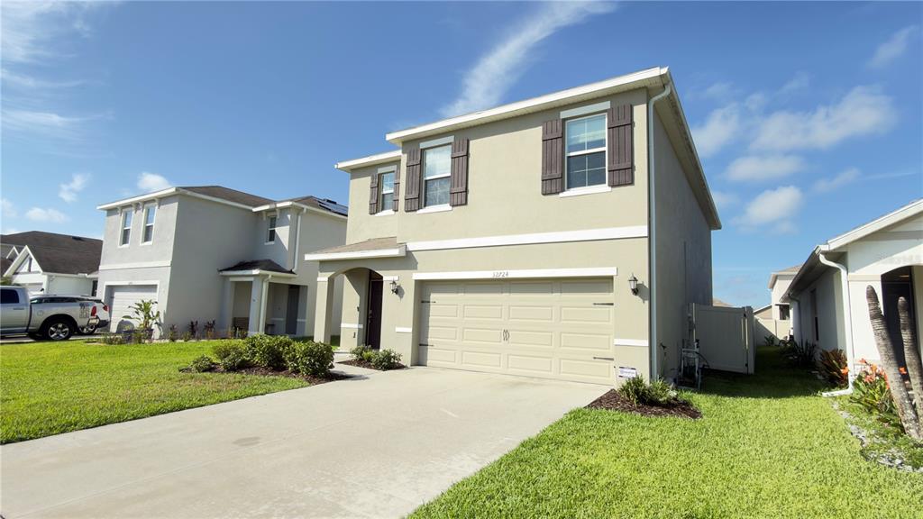 A two-story suburban house with a beige stucco exterior, a two-car garage, and a driveway — 32724 ANSLEY BLOOM LANE, WESLEY CHAPEL, FL