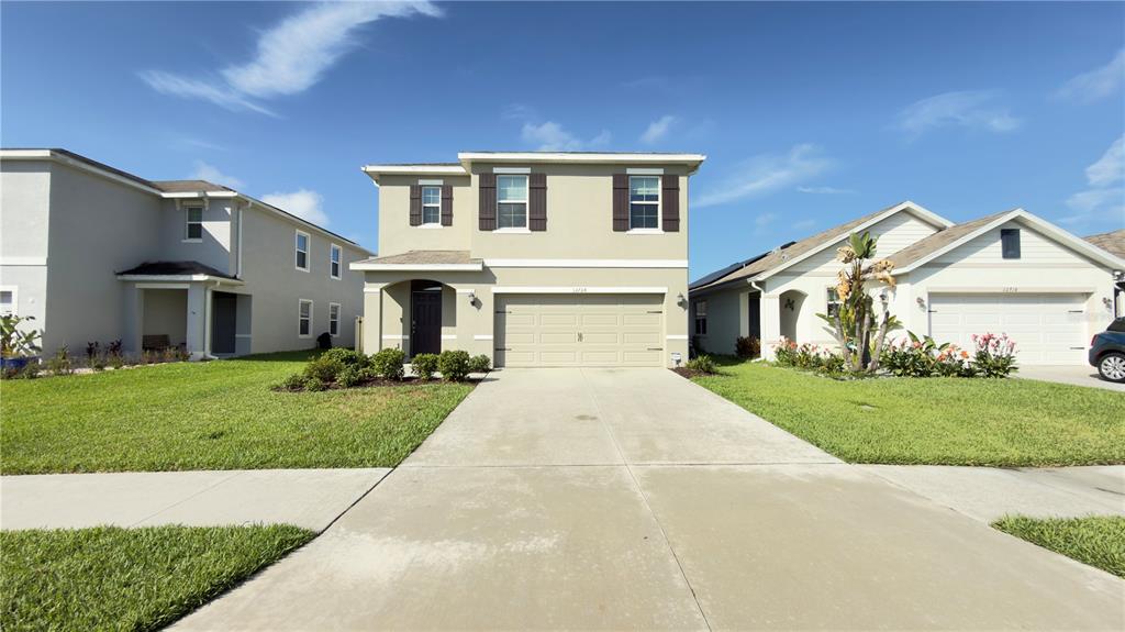 A two-story suburban house with a beige exterior, a two-car garage, and a concrete driveway — 32724 ANSLEY BLOOM LANE, WESLEY CHAPEL, FL