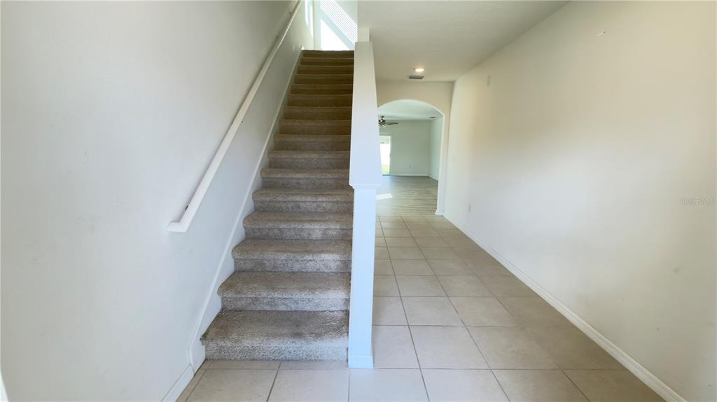 A carpeted staircase sits beside a tiled hallway leading to an arched doorway — 32724 ANSLEY BLOOM LANE, WESLEY CHAPEL, FL