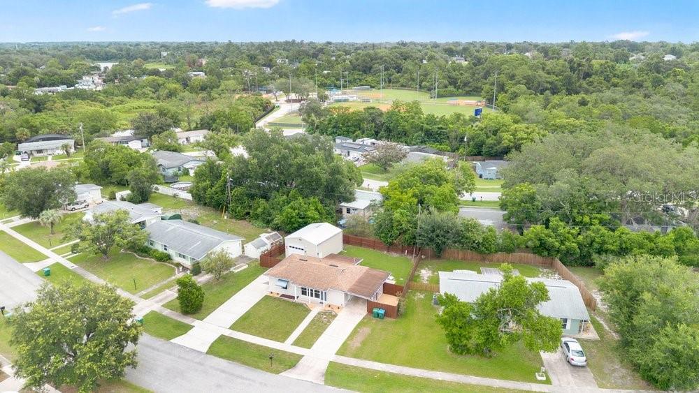 An aerial view shows several single-story houses with lawns and driveways near a wooded park — 1109 COBBLESTONE AVENUE, DELTONA, FL