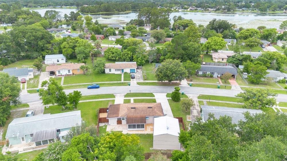 An aerial view of a suburban neighborhood featuring single-story houses, green lawns, and a lake — 1109 COBBLESTONE AVENUE, DELTONA, FL