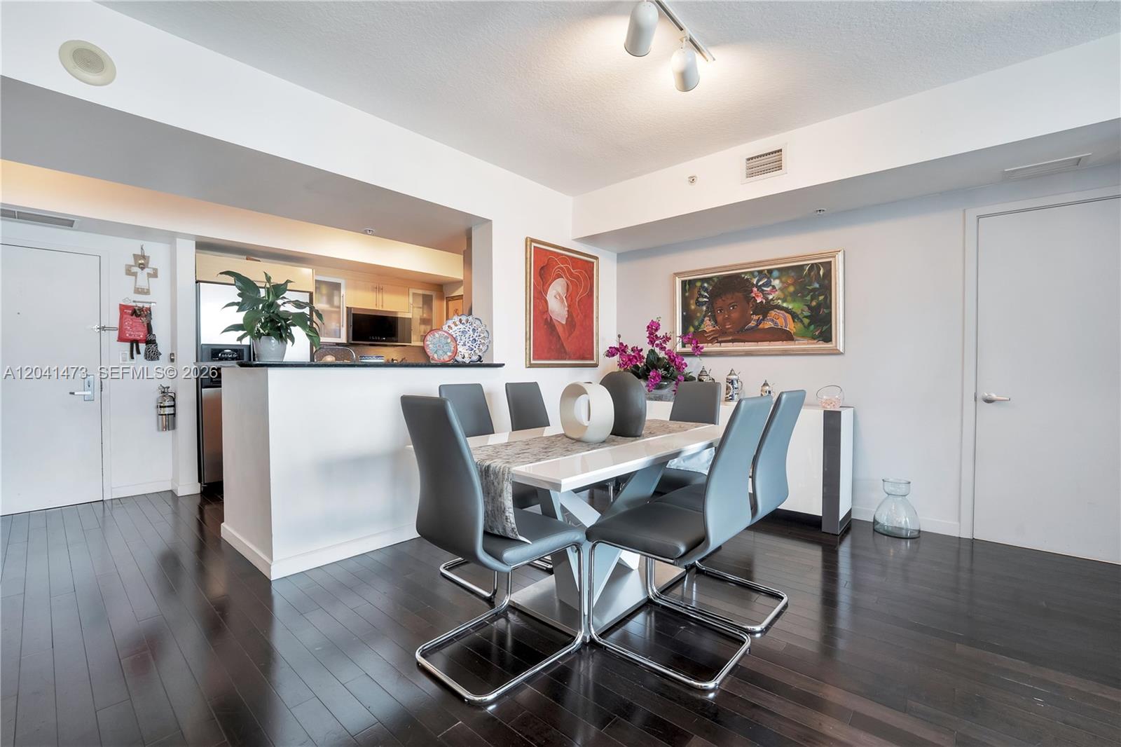 A dining area features a white table with gray chairs, dark wood floors, and wall art — 325 S Biscayne Blvd # 3921, Miami FL 33131, MIAMI, FL