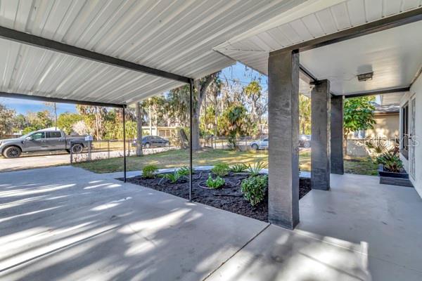 A concrete carport with dark support pillars overlooks a landscaped yard and a residential street — 635 MCCORMICK STREET, DAYTONA BEACH, FL