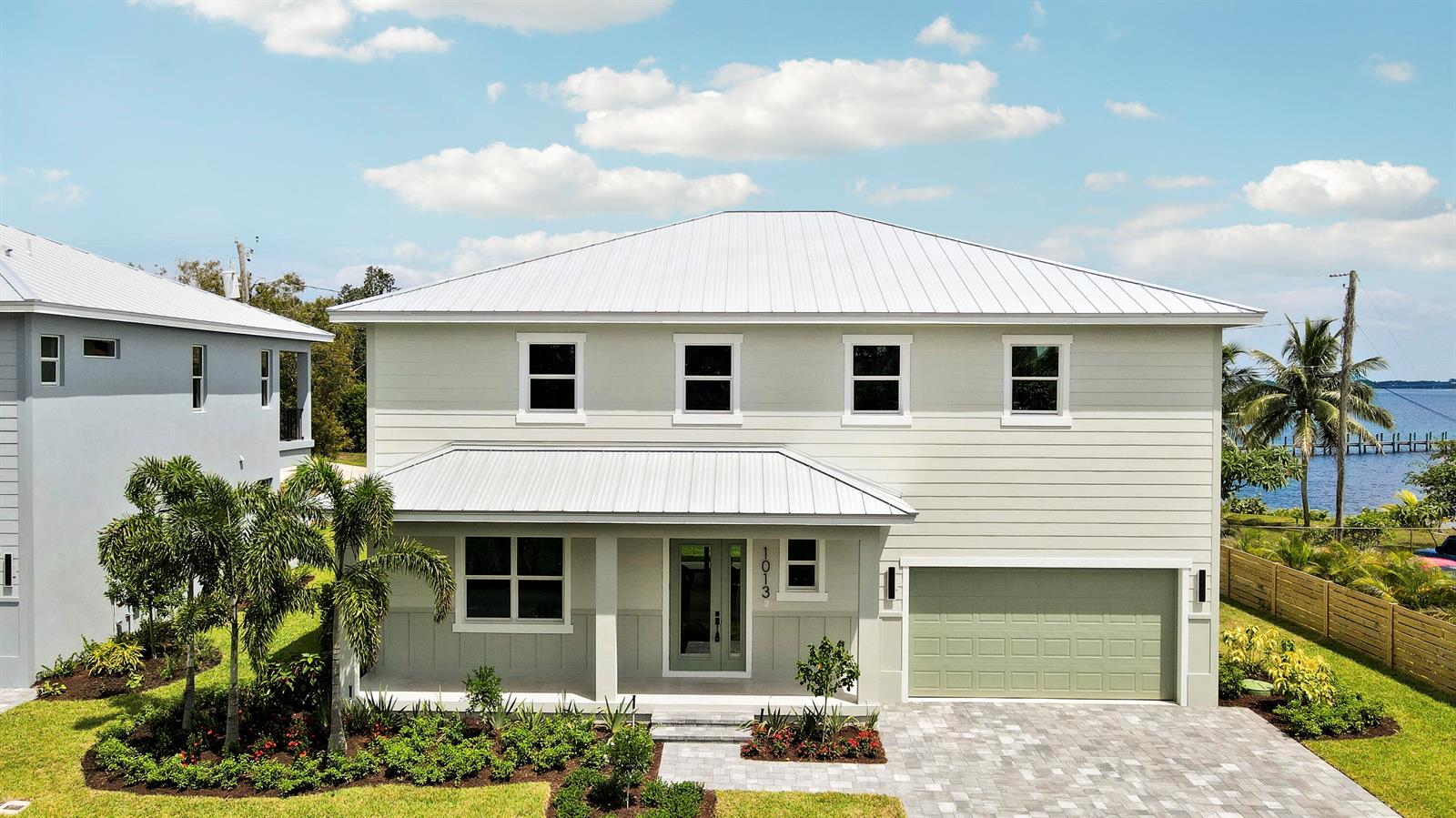 A two-story house with light green siding, a metal roof, and a front-facing garage — 1013 NE Orange Avenue, Jensen Beach FL 34957, JENSEN BEACH, FL
