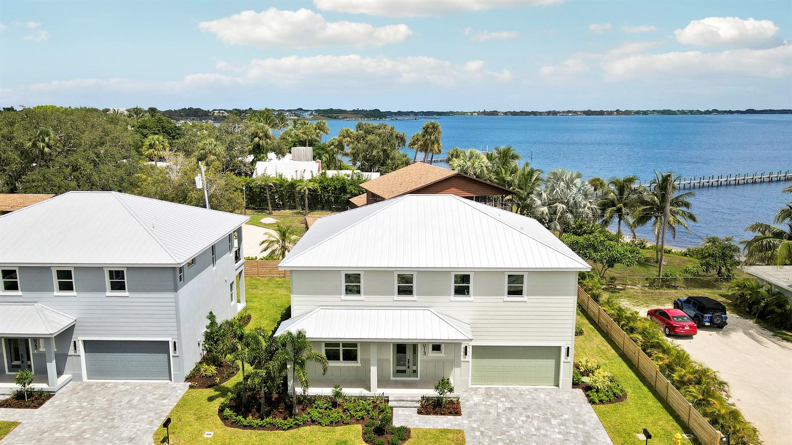 An aerial view shows two modern houses with metal roofs situated near a large lake — 1013 NE Orange Avenue, Jensen Beach FL 34957, JENSEN BEACH, FL