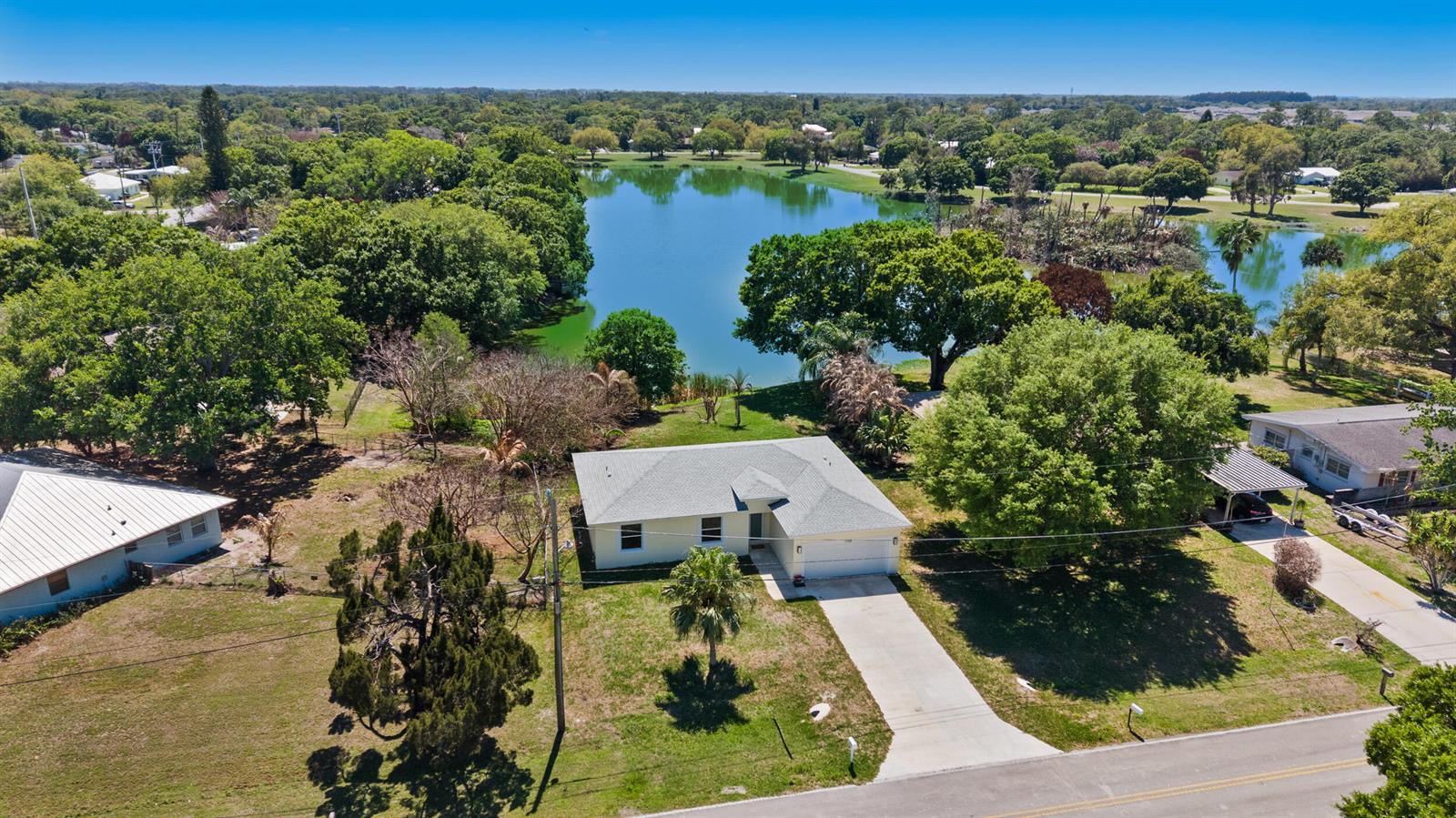 An aerial view shows a single-story house with a driveway situated near a large lake — 7705 Sebastian Road, Fort Pierce FL 34951, FORT PIERCE, FL
