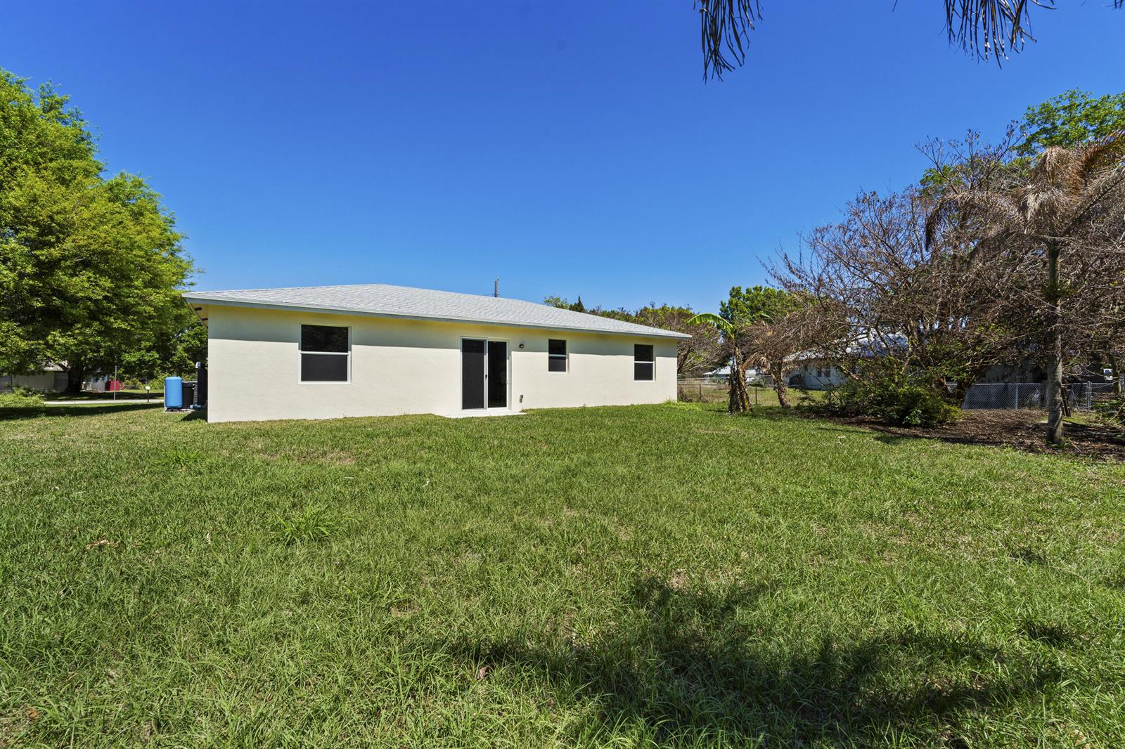The exterior rear view of a single-story house with a lawn and trees — 7705 Sebastian Road, Fort Pierce FL 34951, FORT PIERCE, FL