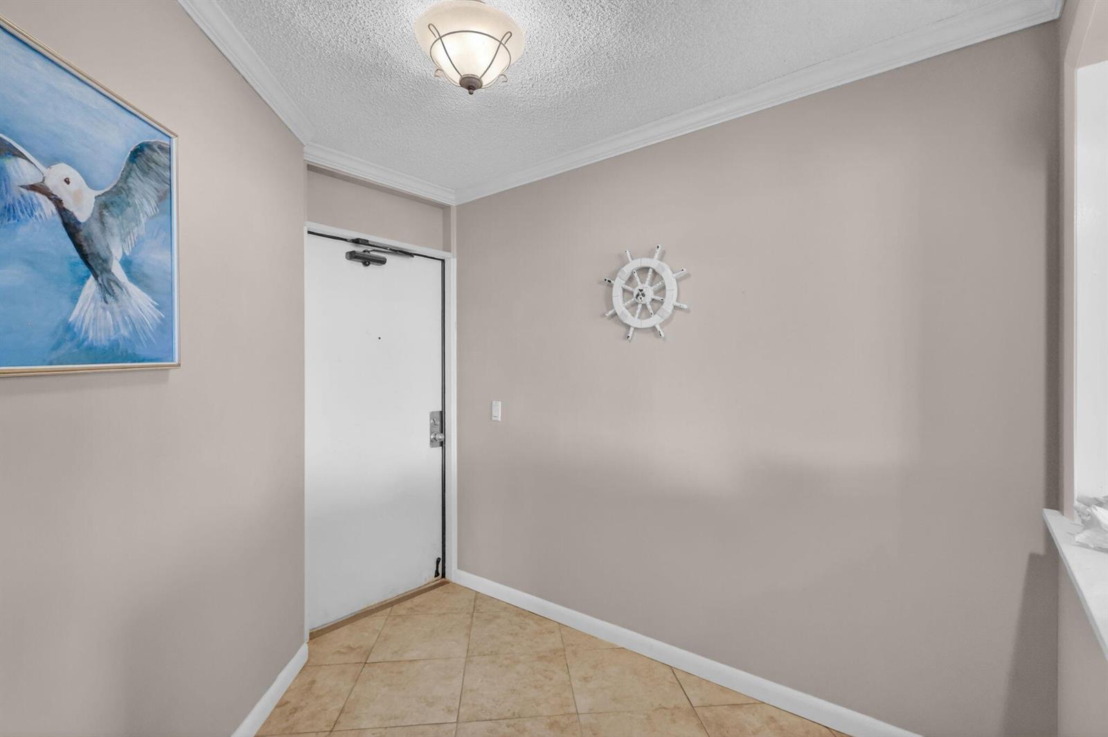 An entryway features beige walls, a tiled floor, a white door, and nautical wall decor — 9650 S Ocean Drive # 210, Jensen Beach FL 34957, JENSEN BEACH, FL