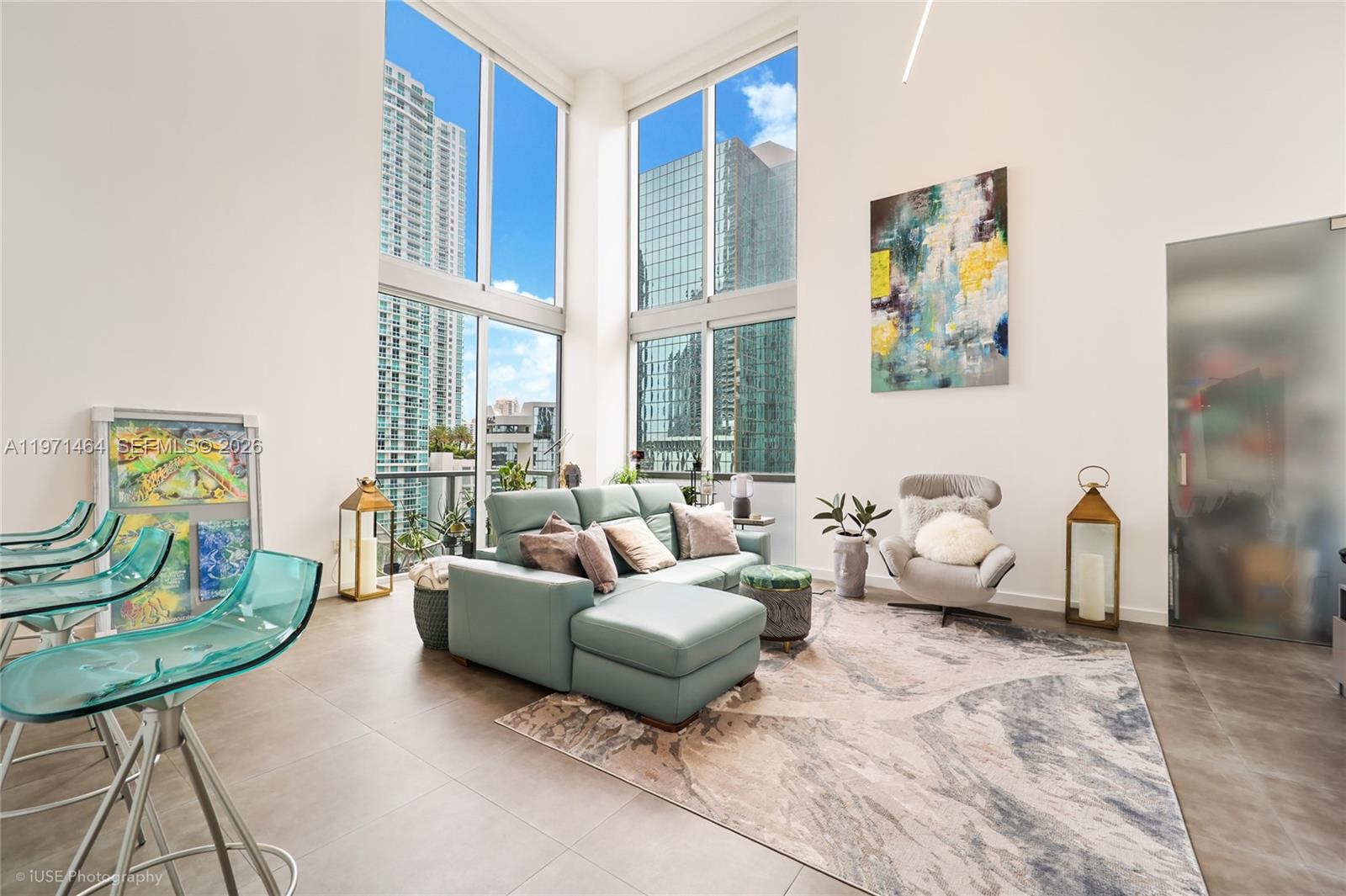 A modern living room features floor-to-ceiling windows, a teal sectional sofa, and tile flooring — 1060 Brickell Ave # 1003, Miami FL 33131, MIAMI, FL
