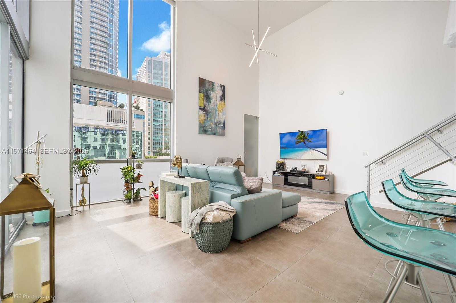 A modern living room features high ceilings, floor-to-ceiling windows, a blue sofa, and tile flooring — 1060 Brickell Ave # 1003, Miami FL 33131, MIAMI, FL